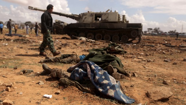 A Libyan rebel walks past dead bodies of