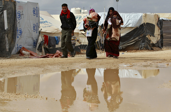 Syrian women, who are refugees, carry their children as they walk with a man at Al- Zaatri refugee camp, in the Jordanian city of Mafraq, near the border with Syria